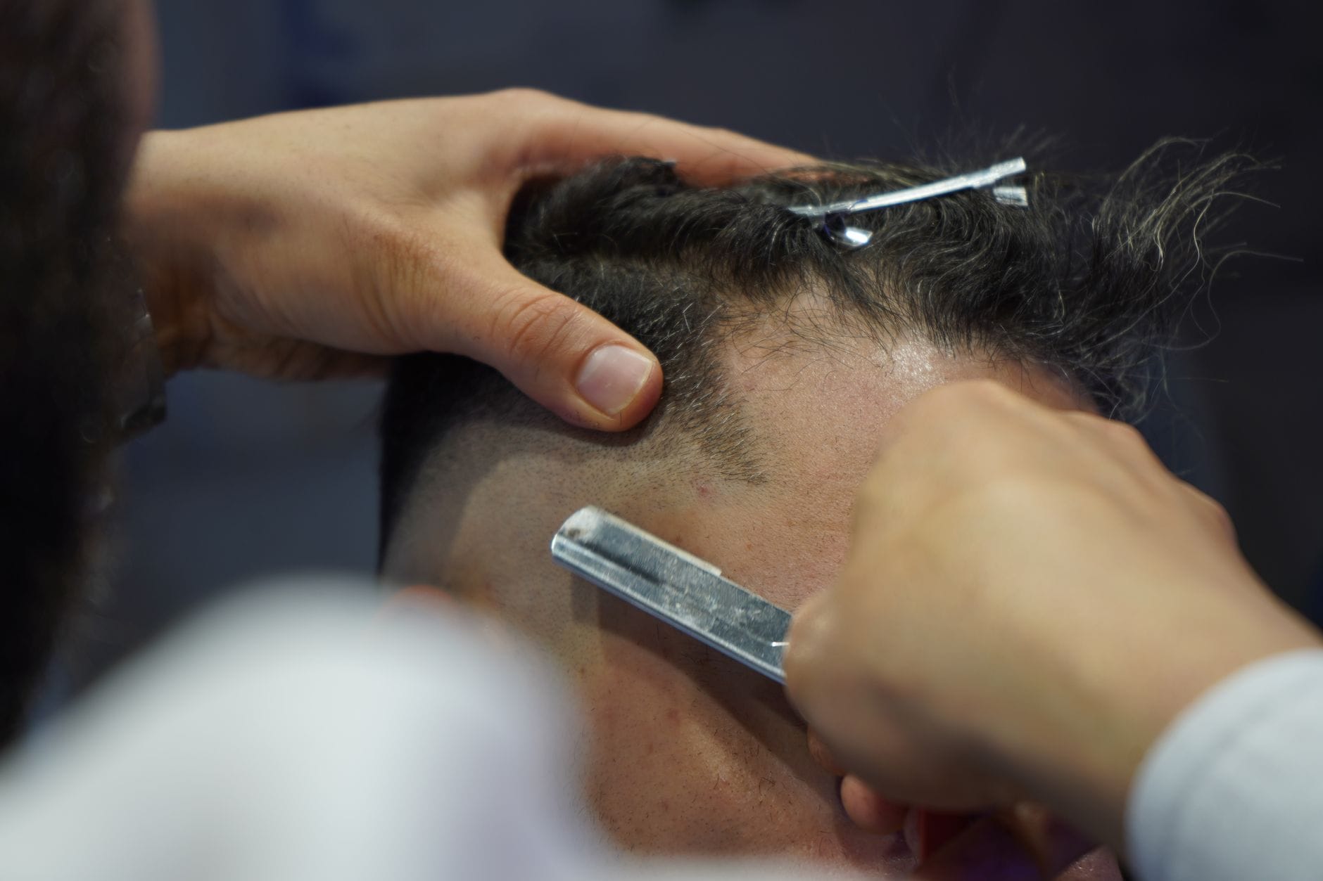 Fryzjer ostrożnie goli głowę klienta brzytwą w salonie