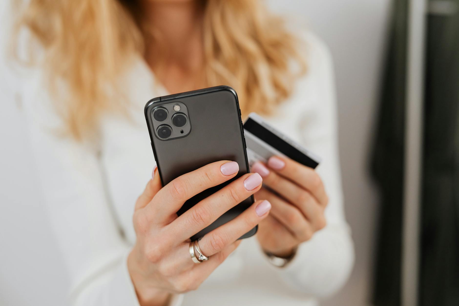 Kobieta w mieszkaniu trzyma smartfon i kartę płatniczą podczas zakupu