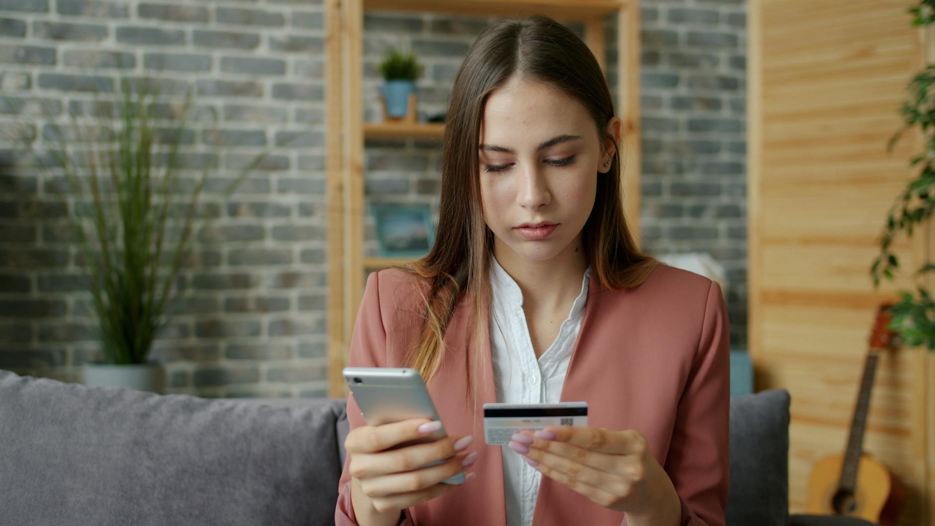 Młoda kobieta w różowej marynarce kupuje smartfon online kartą