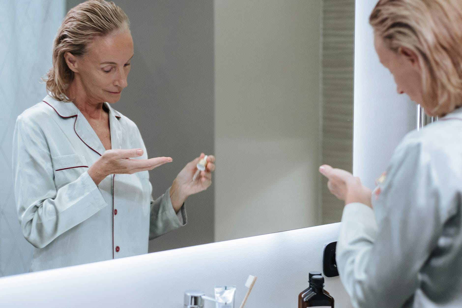 Pielęgnacja po zabiegu a trwałość koloru: co naprawdę ma wpływ na pigment Starsza kobieta nakłada serum pielęgnacyjne przed lustrem w łazience