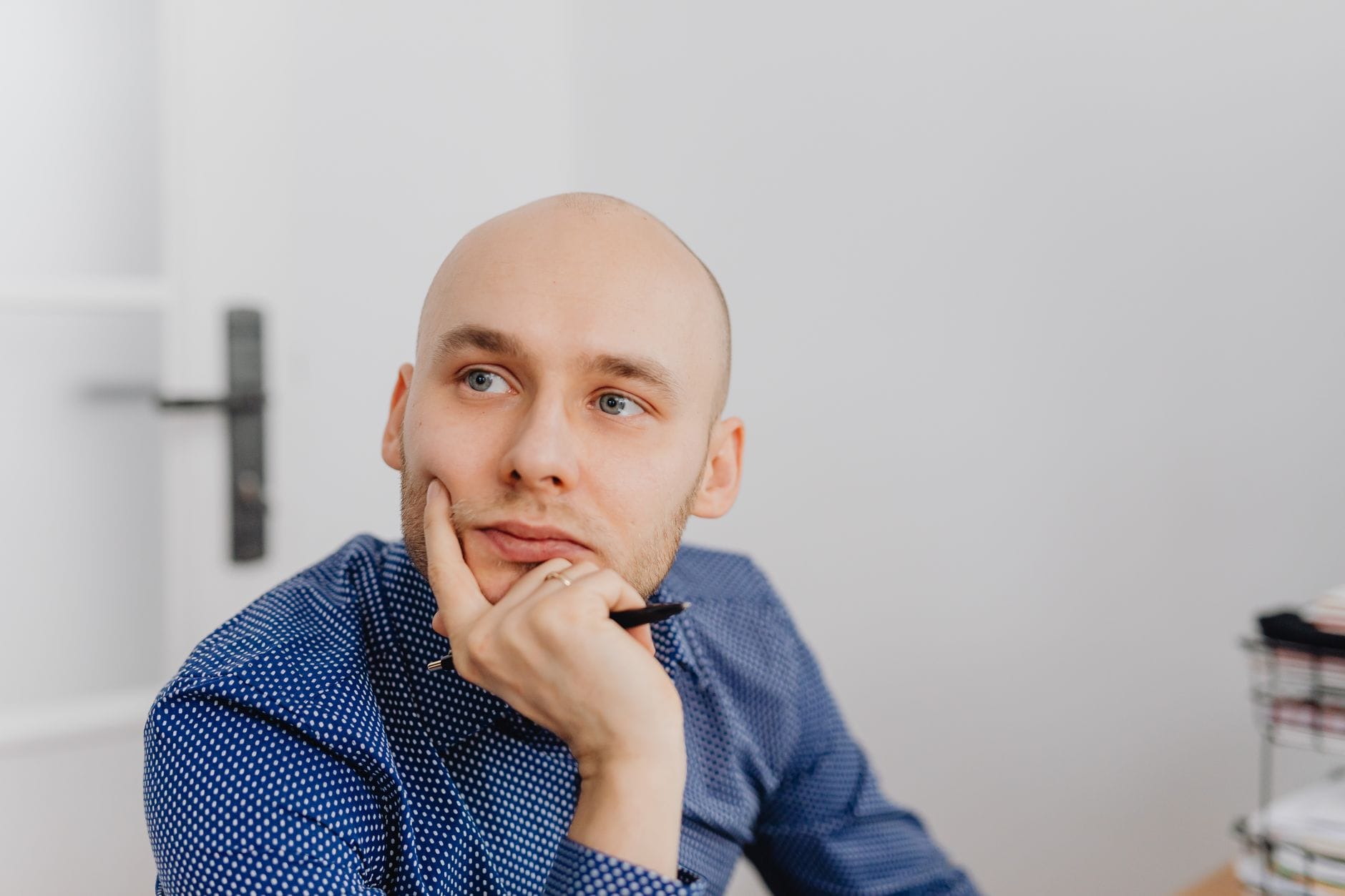 Łysy mężczyzna w niebieskiej koszuli zamyślony przy biurku z długopisem
