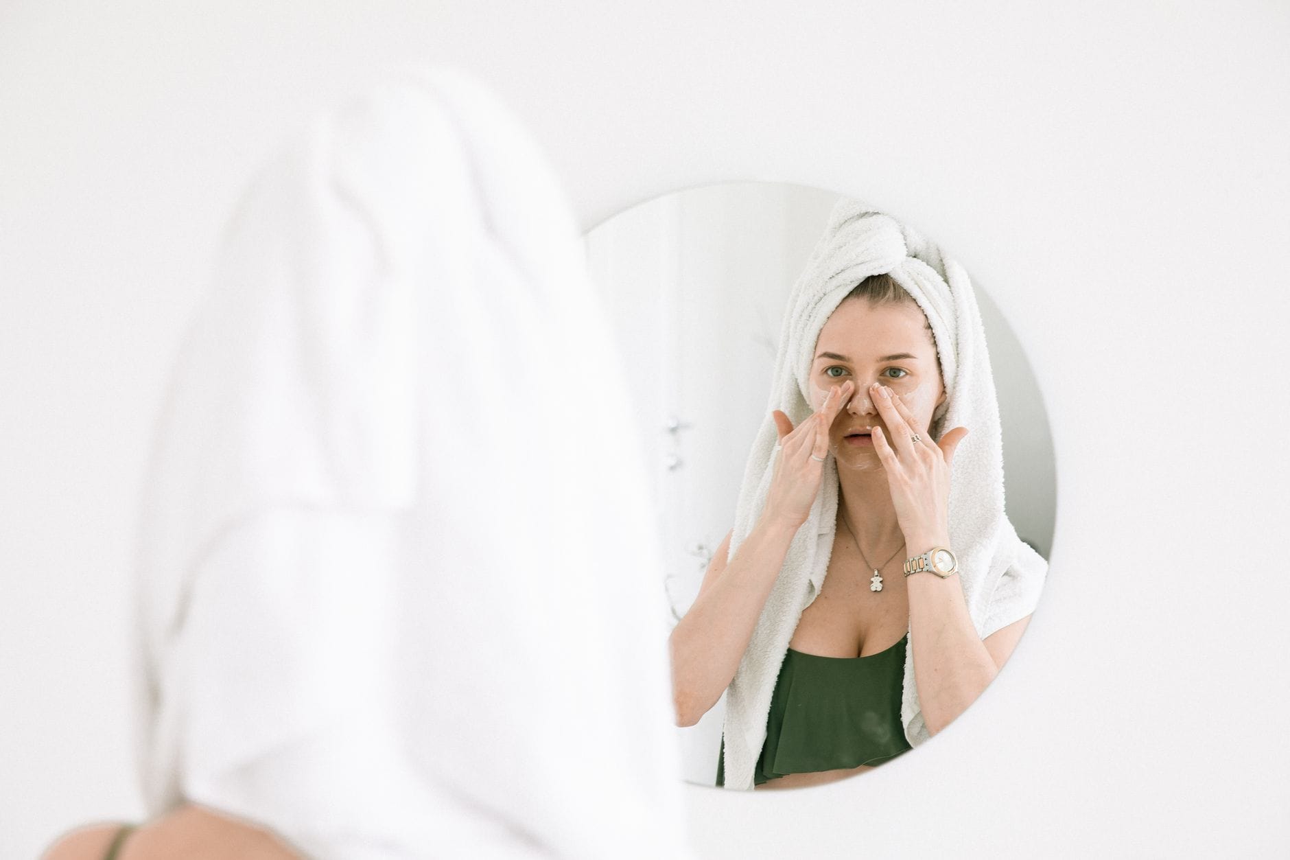 Kobieta w ręczniku wykonuje poranną pielęgnację twarzy przy lustrze Kobieta w ręczniku wykonuje poranną pielęgnację twarzy przy lustrze