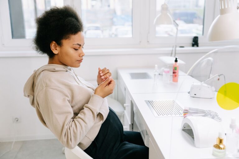Ciężarna kobieta z afro w salonie paznokci ogląda manicure